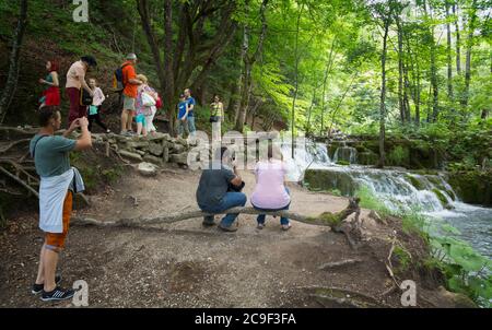 Nationalpark Plitvicer Seen, Lika-Senj County & Karlovac County, Kroatien. Besucher entspannen und fotografieren neben einem kleinen Wasserfall. Stockfoto