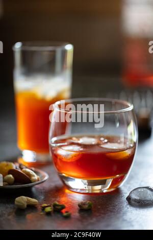 Alkoholische Getränke (Whiskey Wermouth) mit Eis auf dunkler Arbeitsplatte. Gericht mit Knabbereien. Hochformat Stockfoto