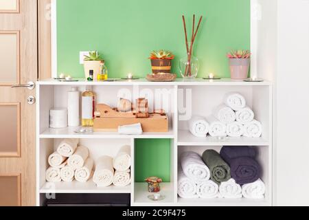 Rollte Badetücher auf dem Regal im Spa-Salon mit Madero Therapie Massage-Tool-Set mit Kerzen und Aloe-Pflanze im häuslichen Interieur dekoriert Stockfoto