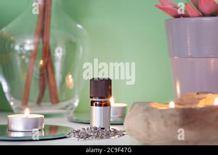 Schöne Komposition mit Lavendelzweig, Cinamon-Sticks, Lavendelöl und brennender weißer Kerze, für Aromatherapie und Entspannung auf einem grünen Hintergrund Stockfoto