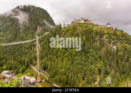 Die Hochlinie179-Fußgängerklappbrücke verläuft von einem Ankerpfeiler im Tal bis zu den Ruinen der Burg Ehrenberg bei Reutte, Tirol, Österreich; ein zweiter Turm der Burganlage ist rechts sichtbar. Die 406 Meter lange Brücke überspannt das Tal in einer Höhe von bis zu 114 Metern und verbindet die Burgruinen mit dem gegenüberliegenden Fort Claudia; von ihrer Eröffnung im Jahr 2014 bis 2017 hielt sie den Guinness-Weltrekord als längste Fußgängerklappbrücke der Welt. Stockfoto