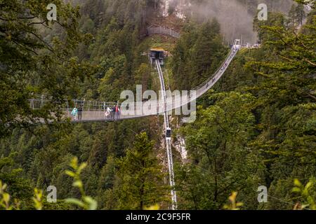 Mehrere Wanderer in bunten Jacken überqueren die Highline179-Fußgängerhängebrücke nahe Reutte, Tirol, Österreich, hoch über das bewaldete Tal. Die 406 Meter lange Brücke überspannt das Tal in einer Höhe von bis zu 114 Metern und verbindet die Ruinen der Ehrenberg-Burg mit dem gegenüberliegenden Fort Claudia; von ihrer Eröffnung im Jahr 2014 bis 2017 hielt sie den Guinness-Weltrekord als längste Fußgängerhängebrücke der Welt. Stockfoto