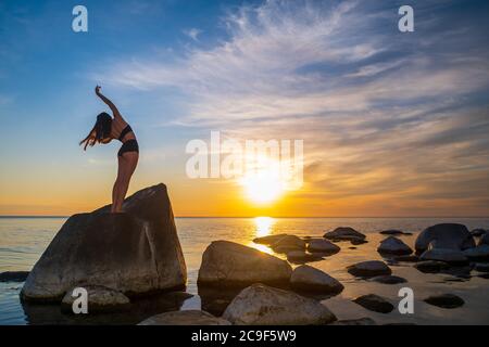 Anonyme Frau tanzt auf Felsen in der Nähe des Meeres Stockfoto