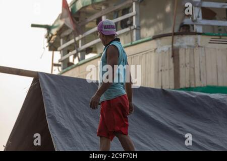 Jakarta, Sunda Kelapa Port, Indonesien - 15. Juli 2019: Ein Mann inspiziert die Ladung eines Schiffes im Hafen von Jakarta und schützt es vor der Sonne und Feuchtigkeit Stockfoto