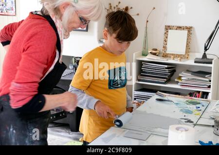 Vivian Kersey, Künstlerin, die den Jungen im Kunstkurs eines Print-Workshop-Studios in Wales, UK, KATHY DEWITT, mit einer Druckwalze Tinte auf die Linoplatte aufträgt Stockfoto