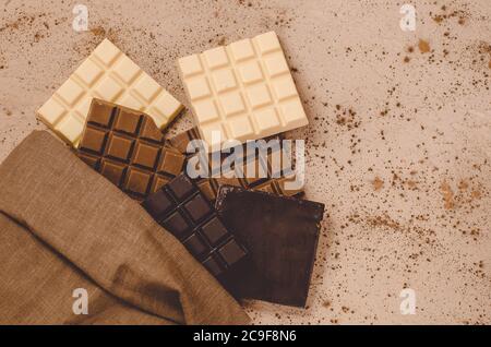 Schokoladen-Süßigkeiten. Schokoriegel in Sackleinen. Verschiedene Milch und dunkle Schokolade. Schokoladenstücke auf Holzhintergrund. Stockfoto