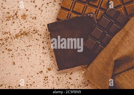 Schokoladen-Süßigkeiten. Schokoriegel in Sackleinen. Verschiedene Milch und dunkle Schokolade. Schokoladenstücke auf Holzhintergrund. Stockfoto