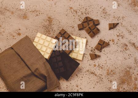 Schokoladen-Süßigkeiten. Schokoriegel in Sackleinen. Verschiedene Milch und dunkle Schokolade. Schokoladenstücke auf Holzhintergrund. Stockfoto