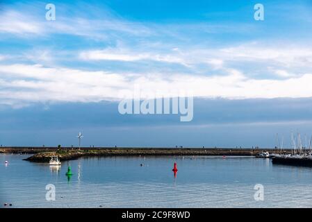 Wellenbrecher mit Fischerschiffen und Menschen in der Nähe im kleinen Handelshafen von Howth, Fischerdorf in der Nähe von Dublin, Irland Stockfoto