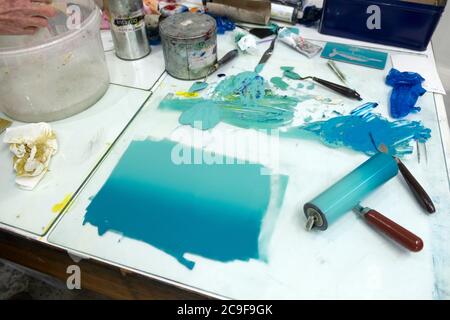Türkisblaue Tinte auf einem Glasoberfläche Tisch mit Walze und Werkzeuge für die Herstellung von Lino Cut Prints in Grafik-Werkstatt Wales UK KATHY DEWITT Stockfoto
