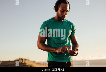 Portrait eines Athleten, der während des morgendlichen Laufs ein Mobiltelefon benutzt. Sportlicher Mann, der Musik über kabellose Kopfhörer hört. Stockfoto