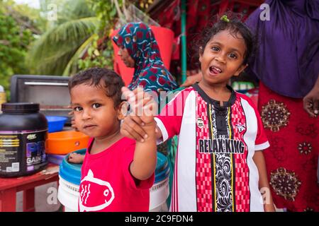 Bodufolhudhoo / Malediven - 17. August 2019: Lächelnde muslimische Kinder blicken auf einen kleinen Wurststand auf der Sandstraße der Malediven Stockfoto