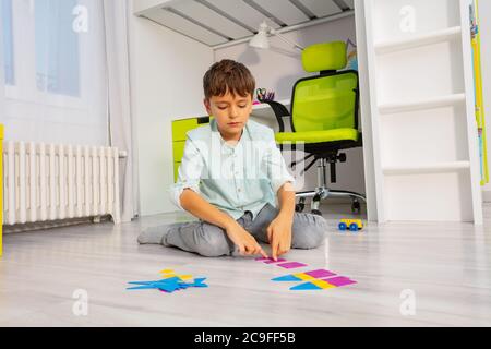 Calm Junge legte geometrische Formen in Ordnung sitzen auf dem Boden im Kinderzimmer Stockfoto