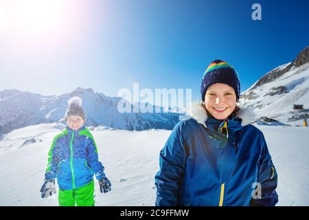 Zwei glückliche Kinder Mädchen mit Jungen haben Spaß stehen zusammen werfen Schnee in der Luft über schöne Aussicht auf die Berge Stockfoto