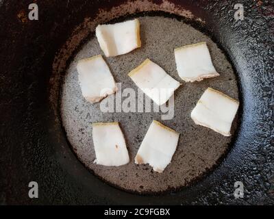 Speckstücke in einer alten schwarzen Bratpfanne anbraten. Stockfoto