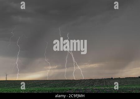 Ein Gewitter bei Sonnenuntergang passiert die Great Plains, während strömender Regen und knackende Blitze den Horizont markieren. Stockfoto