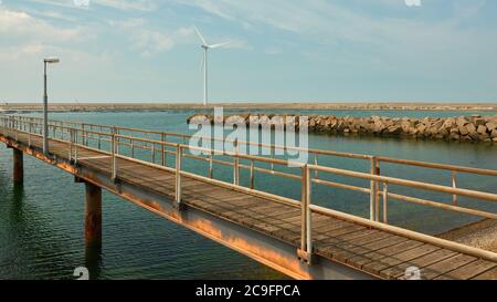 Lange Steg aus Stahl und Holz führt über das Wasser, Steinmole und Windturbine, Muschelfarm kann in der Ferne gesehen werden. Niederlande, Vrouwenpolder. Stockfoto