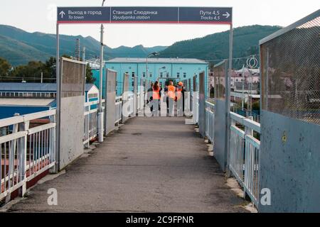 Slyudjanka, Russland - 13. August 2019: Eisenbahner in hellen Spezialwesten gehen entlang der Fußgängerbrücke am Bahnhof Slyudjanka auf der Trans- Stockfoto