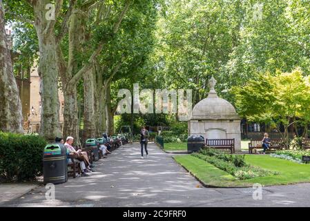 Menschen entspannen auf Parkbänken in Paddington Street Gardens South, Marylebone, London, England, Großbritannien Stockfoto