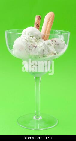 Gefrorene Molkerei Snack und erfrischende Leckerbissen Konzept mit schmelzenden Minze Pistazien Geschmack Eis in Glas Becher isoliert auf grünem Hintergrund Stockfoto