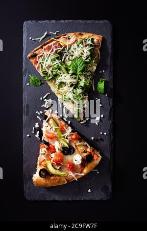 Scheiben heiße Pizza mit Prosciutto, Rucola-Salat, Gemüse, Tomaten und Käse auf Tafel Hintergrund. Draufsicht. Stockfoto