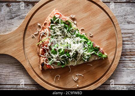 Blick von oben auf die frische Pizzascheibe mit Prosciutto, Rucola und Käse auf Holzbrett. Stockfoto