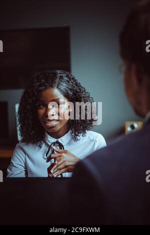 Charmante afrikanische Geschäftsfrau hört seinem männlichen Kollegen zu, der mit dem Rücken im Vordergrund sitzt. Junge afroamerikanische Mädchen Porträt. Unternehmen Stockfoto