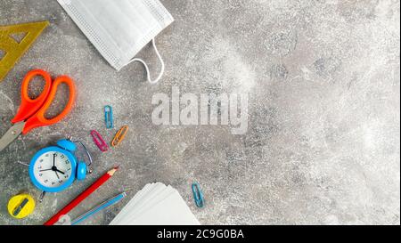 Verschiedene Schreibwaren, blauer Wecker und medizinische Maske. Set von Schulbedarf während Coronavirus Zeit. Lernen zu Hause. Zurück zur Schule Konzept. Bis Stockfoto