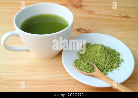 Tasse heißer Matcha Grüner Tee mit einem Teller Matcha Teepulver auf Holztisch Stockfoto