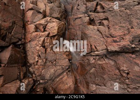 Das reiche, rote Gestein, durchzogen mit Frattenlinien, erlaubt ein kleines Rinnsal an der Seite eines abgelegenen nördlichen Ontario Flusses, der zu den Chippewa Falls an rauscht Stockfoto