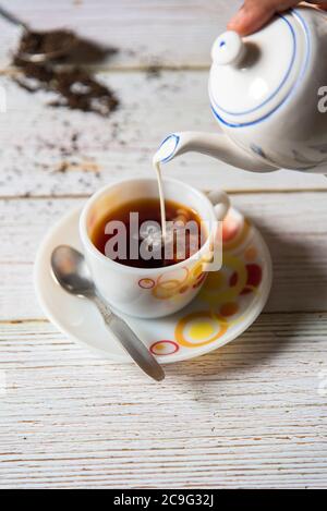 Milch aus Teekanne auf Tasse gießen Stockfoto