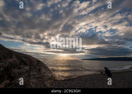 Eine Frau sitzt am Strand im Lake Superior Provincial Park, um den Sonnenuntergang zu beobachten. Stockfoto
