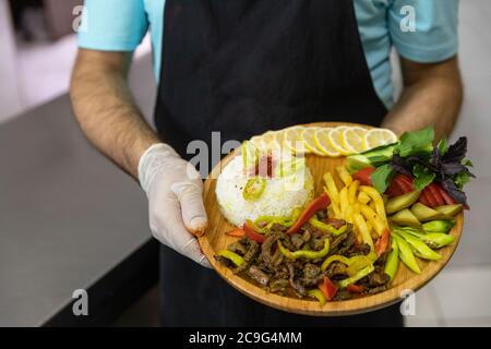 Der Restaurantkoch serviert leckeres Fleischgericht mit Salat, Gemüse auf dem Holzteller Stockfoto