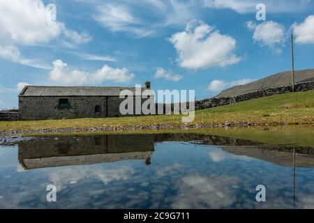 Ungewöhnlicher Blick auf den Berg Pen-y-gent mit einer alten Steinscheune im Vordergrund, die sich in einer Pfütze spiegelt, Yorkshire Dales National Park, England. Stockfoto