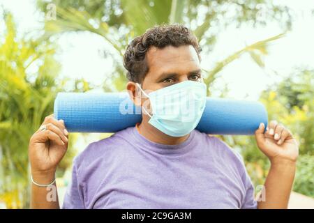 Fat Mann mit medizinischen Gesichtsmaske hält Yoga-Matte auf der Schulter kam für die Übung nach Quarantäne zu parken - Konzept des Lebens nach Coronavirus oder covid Stockfoto