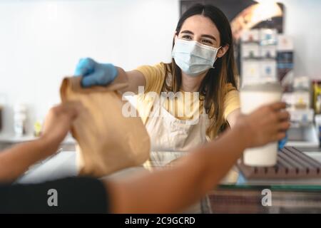 Barbesitzer, der nur mit Bestellungen zum Mitnehmen während des Corona-Virus-Ausbruchs arbeitet - junge Angestellte mit Gesichtsmaske, die Essen zum Mitnehmen gibt Stockfoto