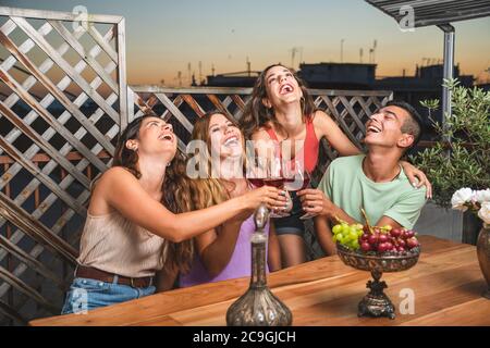Fröhliche Freunde lachen laut und toasten Rotwein zusammen mit weißen und roten schwarzen Trauben auf dem Tisch. Balkon-Konzept mit Freunden, die verbringen Th Stockfoto