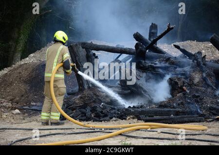 31. Juli 2020 - ein altes Lagerfeuer brennt auf Ackerland in Newchapel bei Lingfield in Surrey. Ein einziges Feuergerät nimmt in weniger als 11 Minuten vom East Grinstead ab und erhält die Kontrolle, um die Ausbreitung auf nahe gelegene Wälder zu verhindern. Die übermäßige Hitze von 32C, starkes Sonnenlicht und starke Brise waren alle Faktoren, die zu seiner Selbstverbrennung und seine Neigung, zu versuchen, Feuer in den Wald zu setzen. Stockfoto