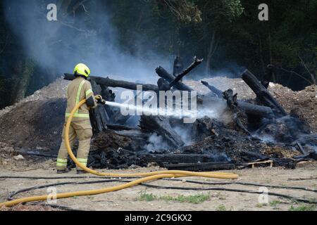 31. Juli 2020 - ein altes Lagerfeuer brennt auf Ackerland in Newchapel bei Lingfield in Surrey. Ein einziges Feuergerät nimmt in weniger als 11 Minuten vom East Grinstead ab und erhält die Kontrolle, um die Ausbreitung auf nahe gelegene Wälder zu verhindern. Die übermäßige Hitze von 32C, starkes Sonnenlicht und starke Brise waren alle Faktoren, die zu seiner Selbstverbrennung und seine Neigung, zu versuchen, Feuer in den Wald zu setzen. Stockfoto