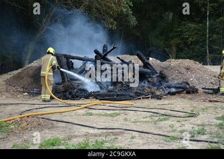 31. Juli 2020 - ein altes Lagerfeuer brennt auf Ackerland in Newchapel bei Lingfield in Surrey. Ein einziges Feuergerät nimmt in weniger als 11 Minuten vom East Grinstead ab und erhält die Kontrolle, um die Ausbreitung auf nahe gelegene Wälder zu verhindern. Die übermäßige Hitze von 32C, starkes Sonnenlicht und starke Brise waren alle Faktoren, die zu seiner Selbstverbrennung und seine Neigung, zu versuchen, Feuer in den Wald zu setzen. Stockfoto