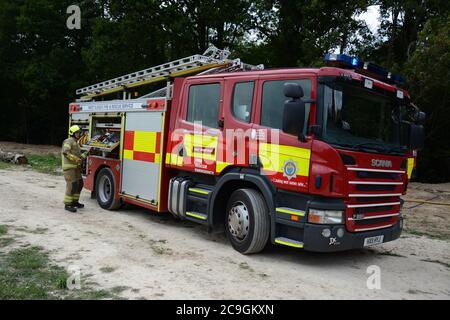 31. Juli 2020 - ein altes Lagerfeuer brennt auf Ackerland in Newchapel bei Lingfield in Surrey. Ein einziges Feuergerät nimmt in weniger als 11 Minuten vom East Grinstead ab und erhält die Kontrolle, um die Ausbreitung auf nahe gelegene Wälder zu verhindern. Die übermäßige Hitze von 32C, starkes Sonnenlicht und starke Brise waren alle Faktoren, die zu seiner Selbstverbrennung und seine Neigung, zu versuchen, Feuer in den Wald zu setzen. Stockfoto