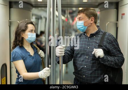 Mann und Frau tragen medizinische Einwegmasken und Gummihandschuhe freundlich reden, während der Fahrt mit der U-Bahn. Vorsichtsmaßnahmen während einer Coronavirus-Pandemie Stockfoto