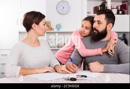 Junger Vater und Mutter unterschreiben Scheidungspapiere, während ihre Tochter zu Hause ist Stockfoto