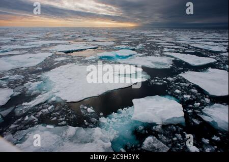 Nördliche arktische Eisschollen werden in dieser Weitwinkelansicht aufgebrochen gesehen, wobei die Sonne am Horizont untergeht.vom Schiff auf See aufgenommen. Stockfoto