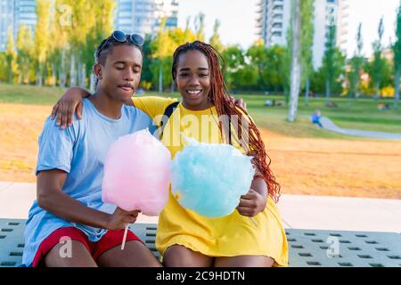 Ein glückliches schwarzes Paar, das bunte Zuckerwatte zusammen in einem Park einer großen Stadt hat. Stockfoto