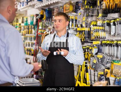 Höflicher Verkäufer, der dem Mann im Baumarkt Werkzeuge anbietet Stockfoto