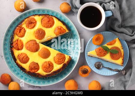 Käsekuchen mit Aprikosen mit einem ausgeschnittenen Stück, auf einem blauen Teller und einer Tasse Kaffee, Draufsicht Stockfoto