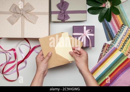 Alles zum Geschenkeinpacken von weiblichen Händen auf weißem Hintergrund. Geschenk-Box mit Schleife. Farbband und Farbpapier. Stockfoto