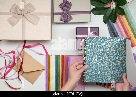 Alles zum Geschenkeinpacken von weiblichen Händen auf weißem Hintergrund. Geschenk-Box mit Schleife. Farbband und Farbpapier. Stockfoto