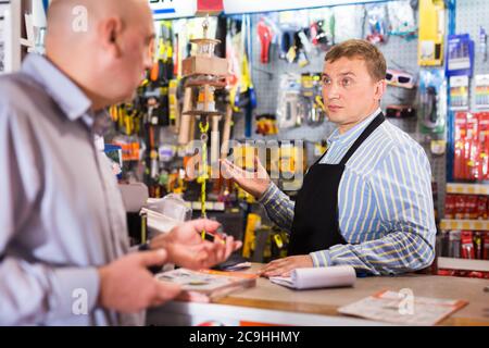 Porträt eines höflichen Verkäufers, der dem Mann im Baumarkt Werkzeuge anbietet Stockfoto